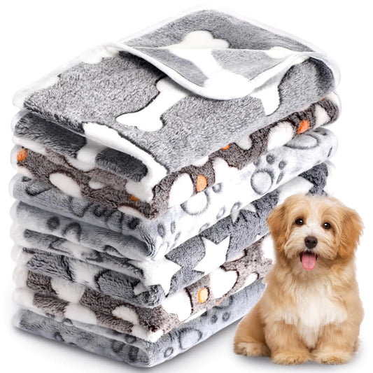 Stack of gray pet blankets with bone and paw patterns next to a small dog.