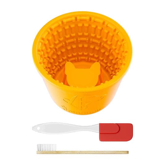 Yellow silicone lick bowl and slow-feeder with textured interior, white and red spatula, and wooden toothbrush on a white background
